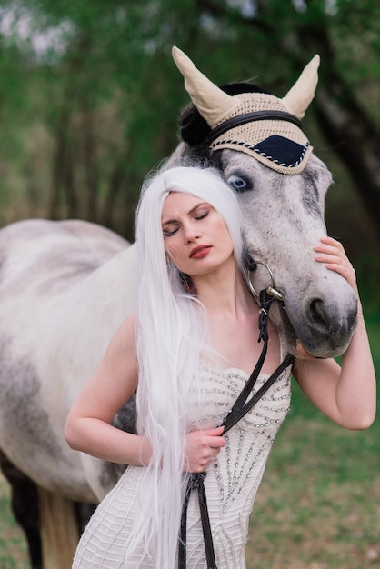 Mulher jovem e atraente com cabelo comprido, perto de um lindo cavalo branco