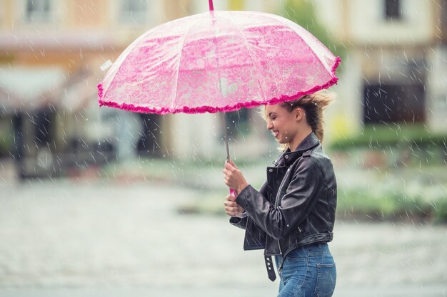 Mulher jovem e atraente com guarda-chuva rosa na chuva e vento forte