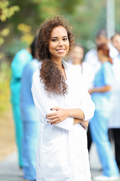 Mulher jovem e atraente com uma área de transferência nas mãos contra um grupo de médicos, ao ar livre