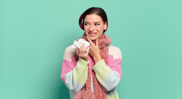 Mulher jovem e atraente de cabelo ruivo sorrindo com uma expressão feliz e confiante com a mão no queixo, pensando e olhando para o conceito de gripe