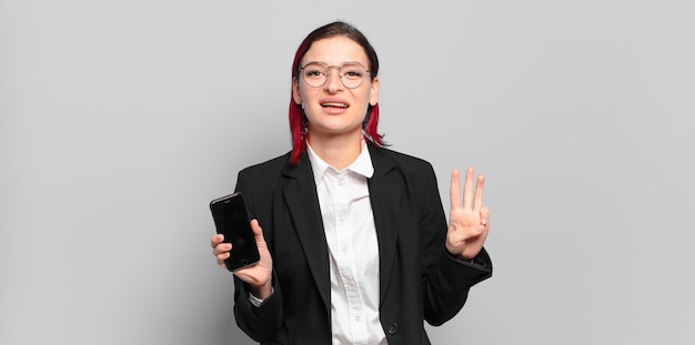 Mulher jovem e atraente de cabelo ruivo sorrindo e parecendo amigável, mostrando o número três ou o terceiro com a mão para a frente