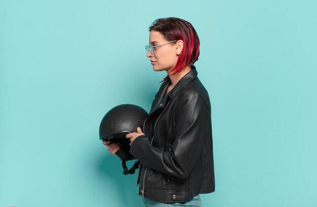 Mulher jovem e atraente de cabelo vermelho em vista de perfil, olhando para copiar o espaço à frente, pensando, imaginando ou sonhando acordado. conceito de motociclista