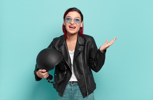 Mulher jovem e atraente de cabelo vermelho se sentindo feliz, animada, surpresa ou chocada, sorrindo e atônita com algo inacreditável. conceito de motociclista