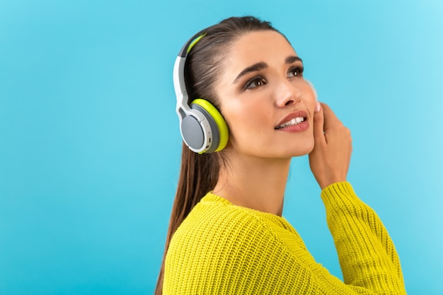 Mulher jovem e atraente e elegante ouvindo música em fones de ouvido sem fio feliz vestindo suéter de malha amarela colorido estilo posar