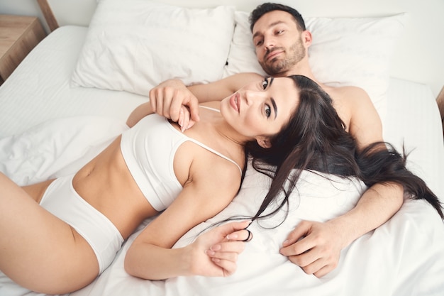Foto mulher jovem e atraente e relaxada em lingerie deitada na cama ao lado do marido bonito e sereno