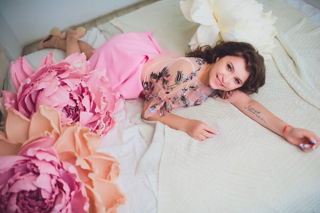 Mulher jovem e atraente elegante vestido sentado no interior decorado com flores. Linda garota sorridente fresca posando com flores