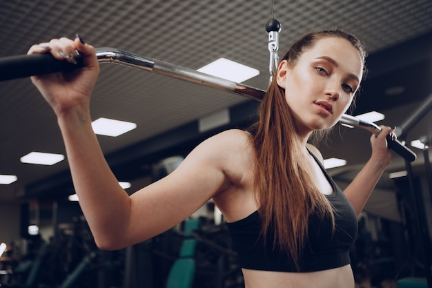 Mulher jovem e atraente fazendo exercícios para os músculos dos braços e costas em uma academia