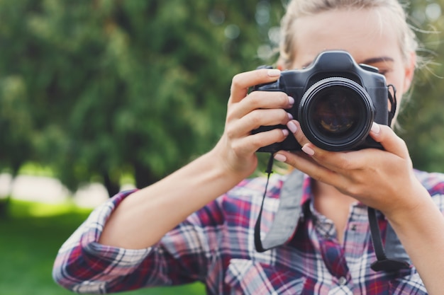 Mulher jovem e atraente fotografando com uma câmera profissional ao ar livre, copie o espaço. Tirando fotos e conceito de aulas de fotografia