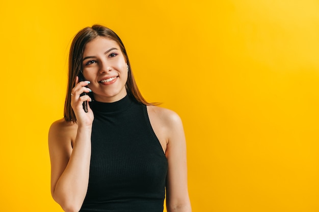 Mulher jovem e atraente morena falando com alguém usando um telefone celular e sorrindo