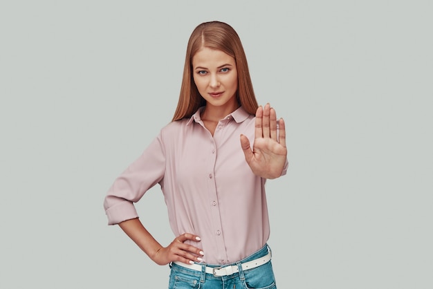 Mulher jovem e atraente mostrando um gesto de parada em pé contra um fundo cinza