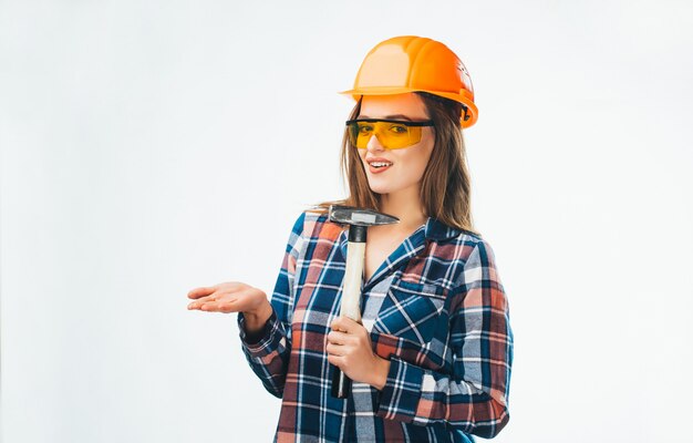 Mulher jovem e atraente na construção de capacete com martelo e óculos de proteção laranja com branco