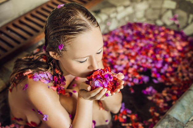 Mulher jovem e atraente no banho com pétalas de flores tropicais e óleos aromáticos. Tratamentos de spa para rejuvenescimento da pele. Mulher sedutora no salão Spa. Garota relaxante no jacuzzi com pétalas de flores. sp de luxo