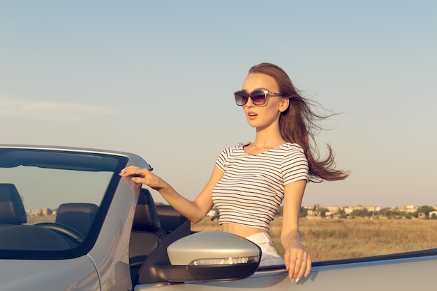 Mulher jovem e atraente perto de um carro conversível