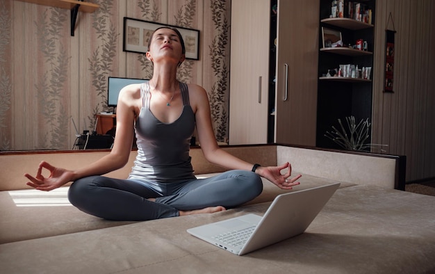 Mulher jovem e atraente se exercitando e sentada em posição de lótus de ioga enquanto descansava em casa