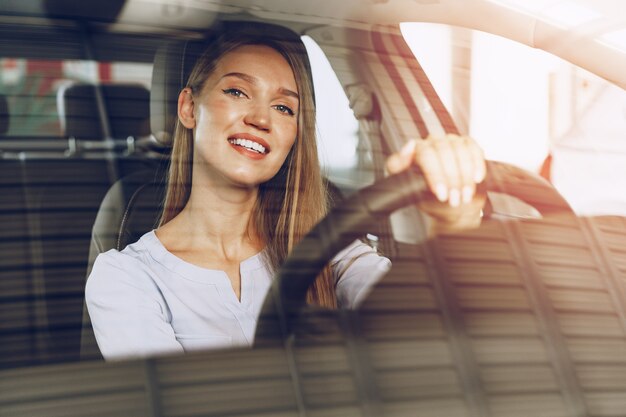 Foto mulher jovem e atraente sentada em um carro novo no showroom close-up