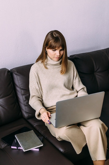 Mulher jovem e atraente trabalhando em um laptop no sofá. a blogueira feminina trabalha em casa. trabalho remoto.