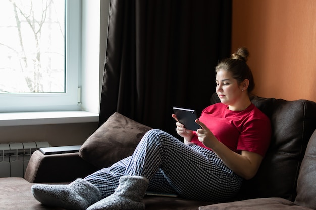 Mulher jovem e atraente usa computador tablet enquanto está sentado no sofá da sala em casa.