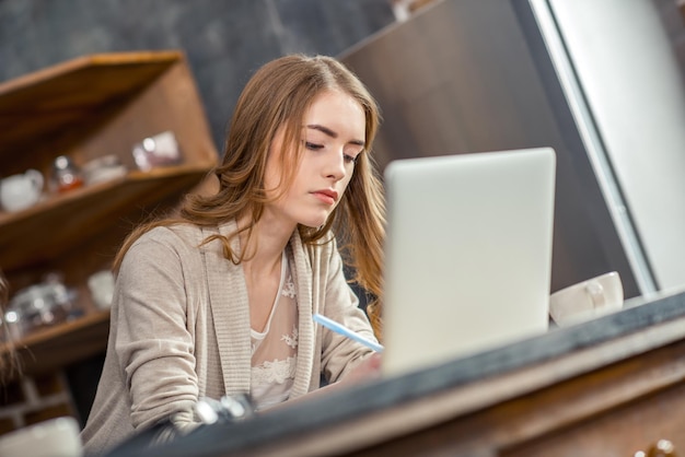 Mulher jovem e atraente usando laptop e escrevendo com caneta
