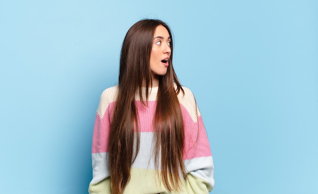 Mulher jovem e bem casual se sentindo chocada, feliz, maravilhada e surpresa, olhando para o lado com a boca aberta