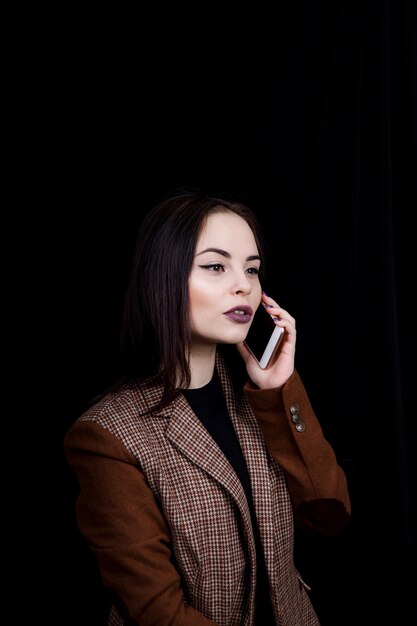 Mulher jovem e bem-sucedida, alegre e bem-sucedida, está falando emocionalmente ao telefone. Mulher jovem e bonita em uma jaqueta cinza casual segurando um smartphone