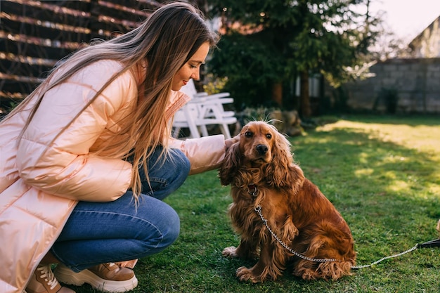 Mulher jovem e bonita acaricia seu cachorro no prado verde fresco