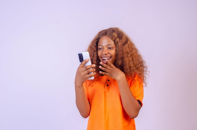 Mulher jovem e bonita africana usando seu telefone, parecendo surpresa e animada