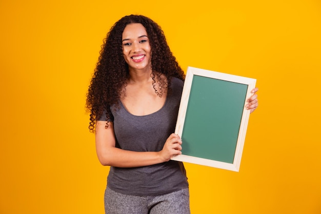 Mulher jovem e bonita afro segurando uma lousa com espaço livre para texto.