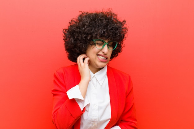 Mulher jovem e bonita afro sentindo estressado frustrado e cansado, esfregando o pescoço doloroso com um olhar preocupado e preocupado