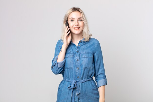 Mulher jovem e bonita albina parecendo feliz e agradavelmente surpresa e falando com um smartphone