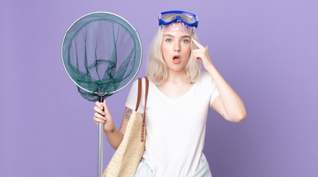 Mulher jovem e bonita albina parecendo surpresa, percebendo um novo pensamento, ideia ou conceito com óculos e uma rede de pesca