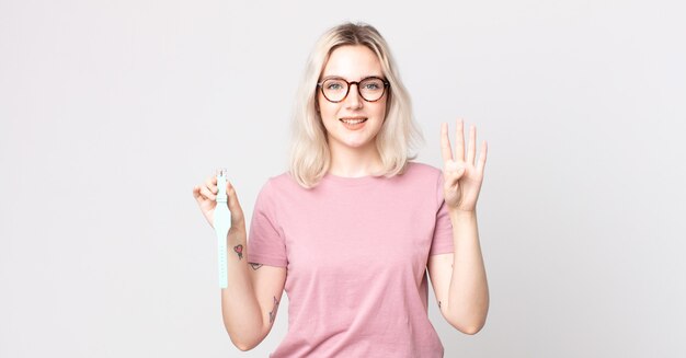 Mulher jovem e bonita albina sorrindo e parecendo amistosa, mostrando o número quatro segurando um relógio de pulso