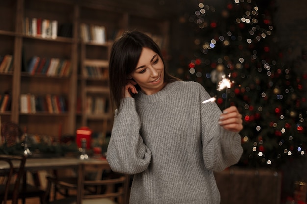 Mulher jovem e bonita alegre com uma camisola de malha na moda está segurando um diamante da árvore de Natal em um quarto vintage. Atmosfera mágica de ano novo. Linda garota.