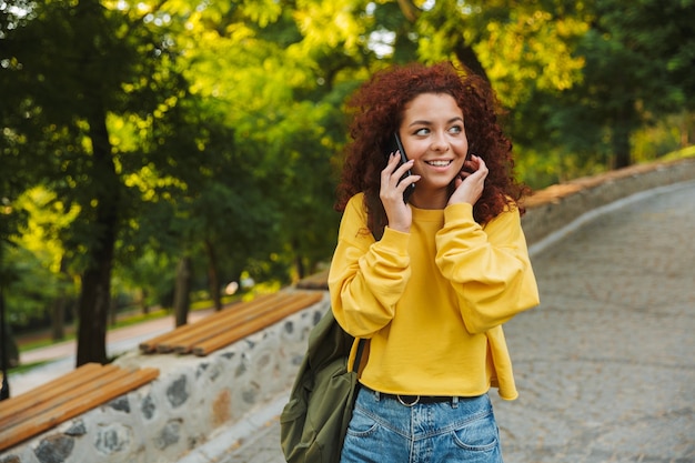 Mulher jovem e bonita alegre passando um bom tempo no parque, falando no celular