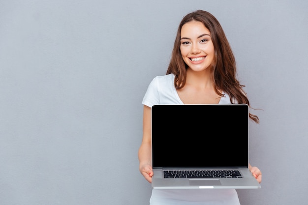 Mulher jovem e bonita alegre segurando um laptop de tela em branco