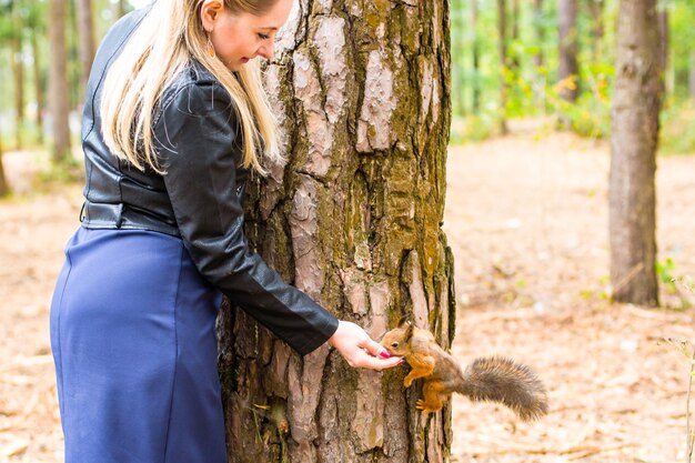 Mulher jovem e bonita alimentando um esquilo em um parque de outono