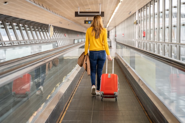 Mulher jovem e bonita andando para trás para o aeroporto ou estação com sua bagagem