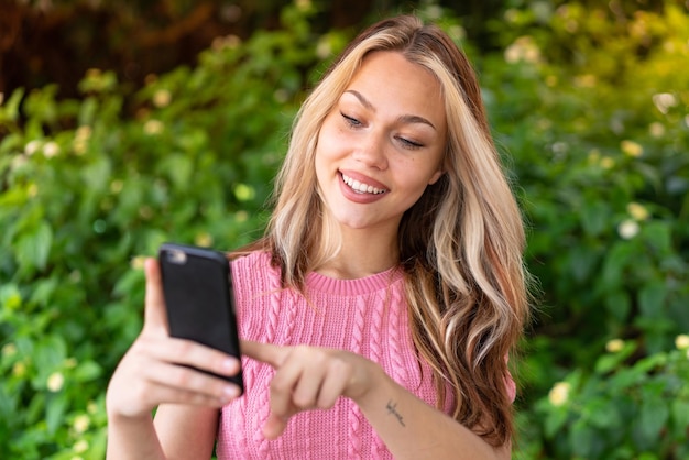 Mulher jovem e bonita ao ar livre enviando uma mensagem ou e-mail com o celular