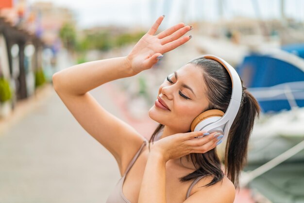 Foto mulher jovem e bonita ao ar livre ouvindo música e dançando