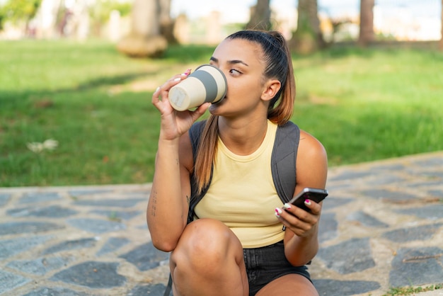 Mulher jovem e bonita ao ar livre usando telefone celular e segurando um café para levar