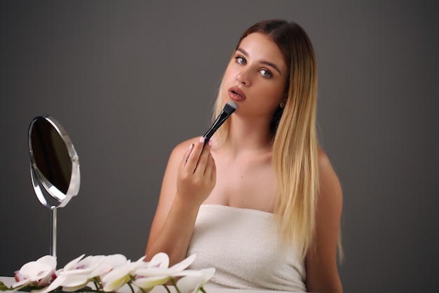 Foto mulher jovem e bonita aplicando maquiagem no banheiro.