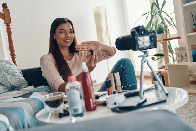 Mulher jovem e bonita apontando para um produto de beleza e sorrindo enquanto faz um vídeo nas redes sociais