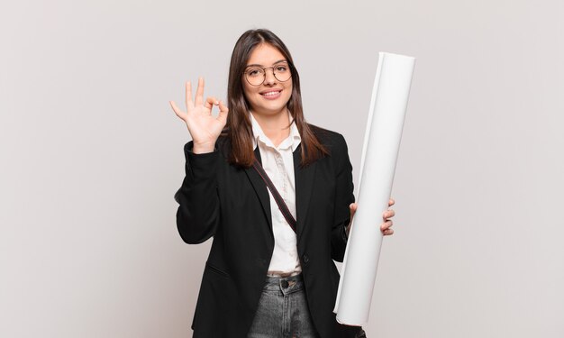 Mulher jovem e bonita arquiteta se sentindo feliz, relaxada e satisfeita, mostrando aprovação com um gesto de ok, sorrindo