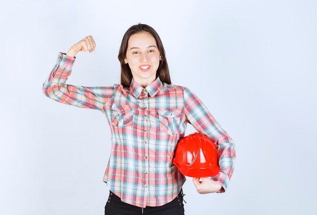 Mulher jovem e bonita arquiteto segurando capacete de segurança sobre uma parede branca.