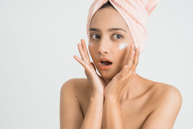 Mulher jovem e bonita asiática aplicando creme cosmético no rosto