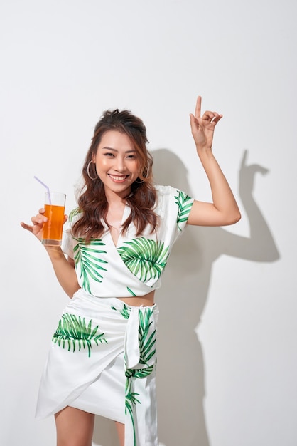 Mulher jovem e bonita asiática com suco de laranja em uma camisa tropical em fundo branco