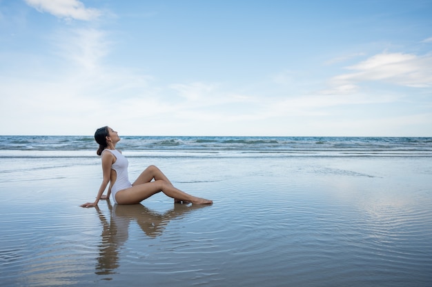 Mulher jovem e bonita asiática em traje de banho relaxando e tomando banho de sol na praia em um mar tropical nas férias