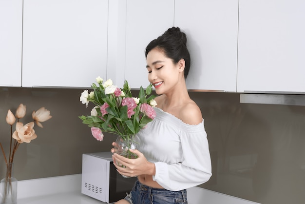 Mulher jovem e bonita asiática posando com flores na cozinha.