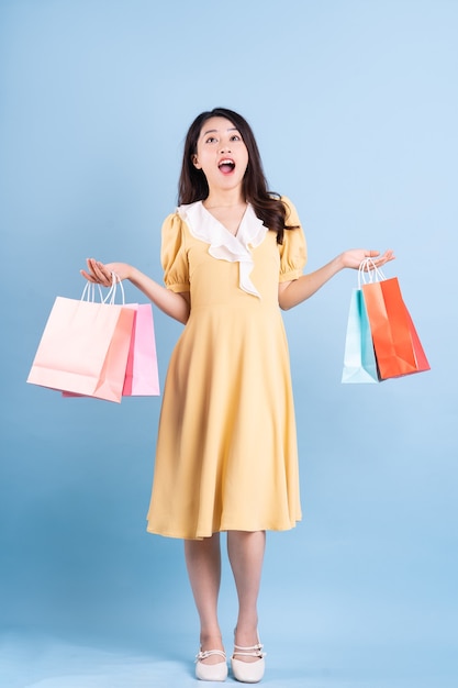 Mulher jovem e bonita asiática segurando uma sacola de compras sobre fundo azul