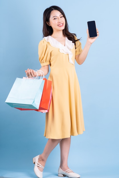 Mulher jovem e bonita asiática segurando uma sacola de compras sobre fundo azul