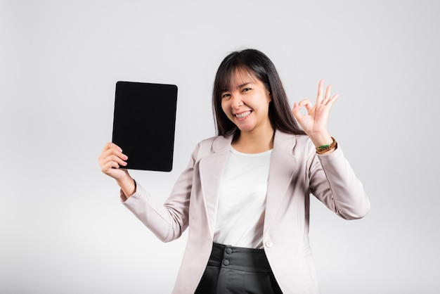 Mulher jovem e bonita asiática sorrindo usando computador tablet, mulher feliz mostra tablet digital de tela em branco e mostra OK cante para aceitar, tiro de estúdio isolado no fundo branco